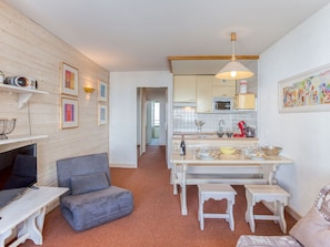 A compact living space with a kitchenette, a grey sofa, a small dining table, and a white bench.