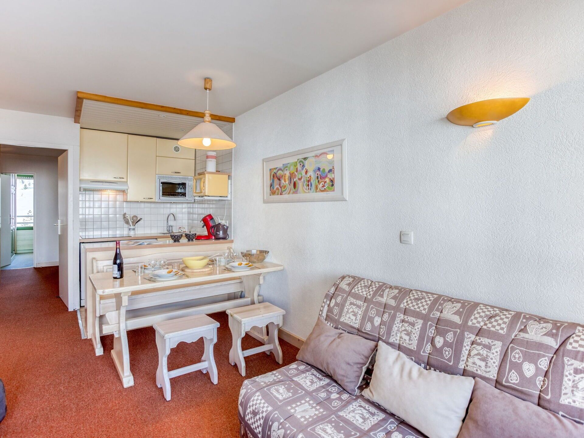 A compact living space with a kitchenette, a dining area, and a sofa with patterned cushions.