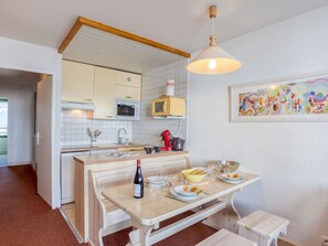 A compact kitchen with a microwave, oven, and sink. There is a dining table with chairs and a bench, and a small stool. A bottle of wine and glasses are on the table. - Lovely apartment for 6 people with WIFI, TV, balcony and panoramic view (Les Boisses)