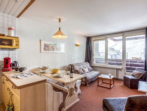 A cozy living room with a sofa, a coffee table, and a dining area with a table and chairs. There is a window with a view of a snowy landscape. - Lovely apartment for 6 people with WIFI, TV, balcony and panoramic view (Les Boisses)
