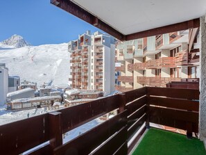 Varanda com guarda-mão de madeira com vista para uma montanha nevada e um edifício com várias varandas.