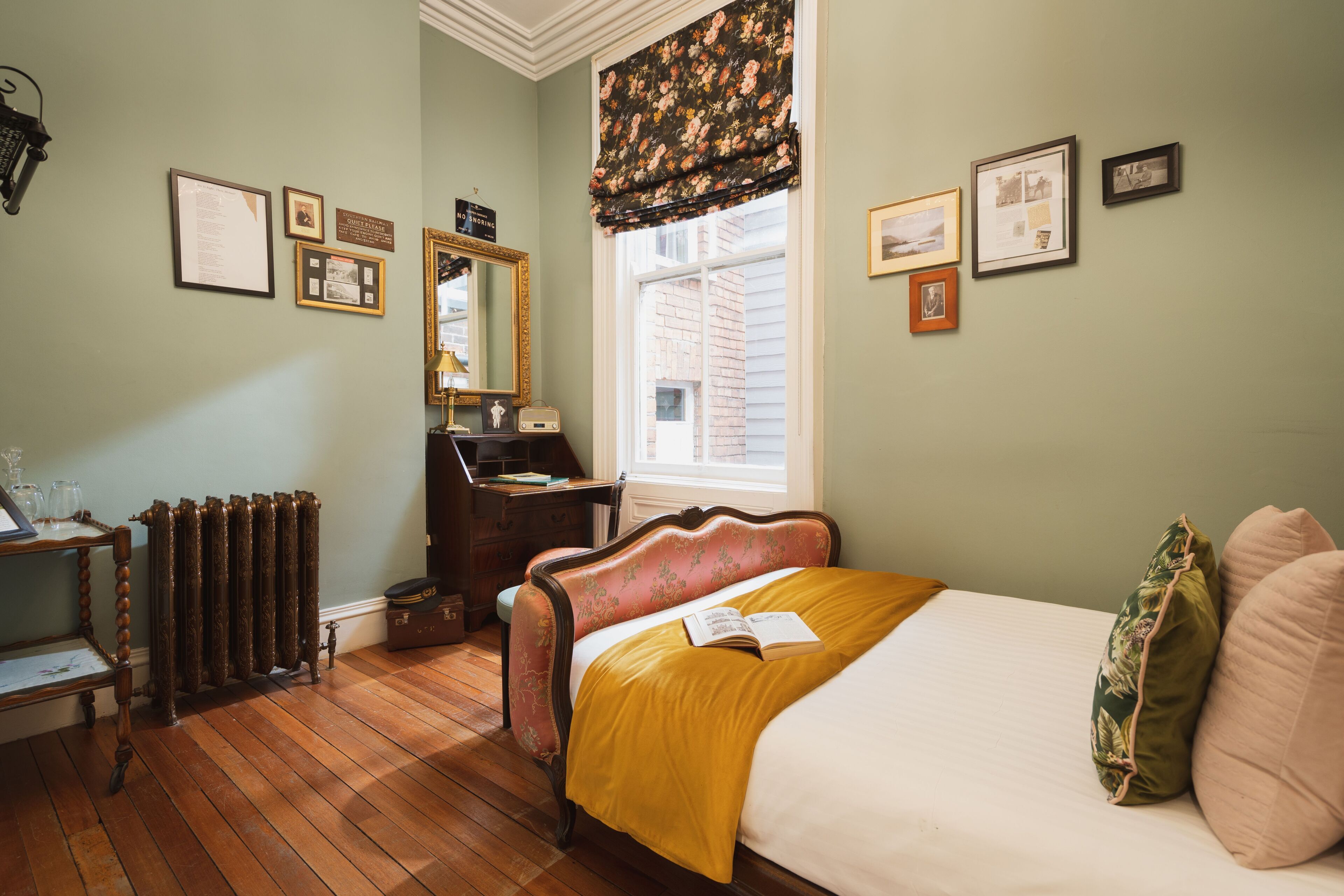 A bedroom with a wooden floor, a bed with a yellow blanket, a dresser, a mirror, and framed pictures on the wall.