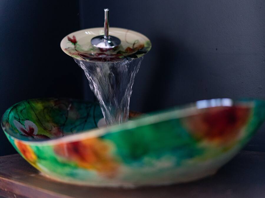 Un tazón de vidrio decorativo con motivos florales y una fuente de agua de vidrio transparente con un caño metálico.