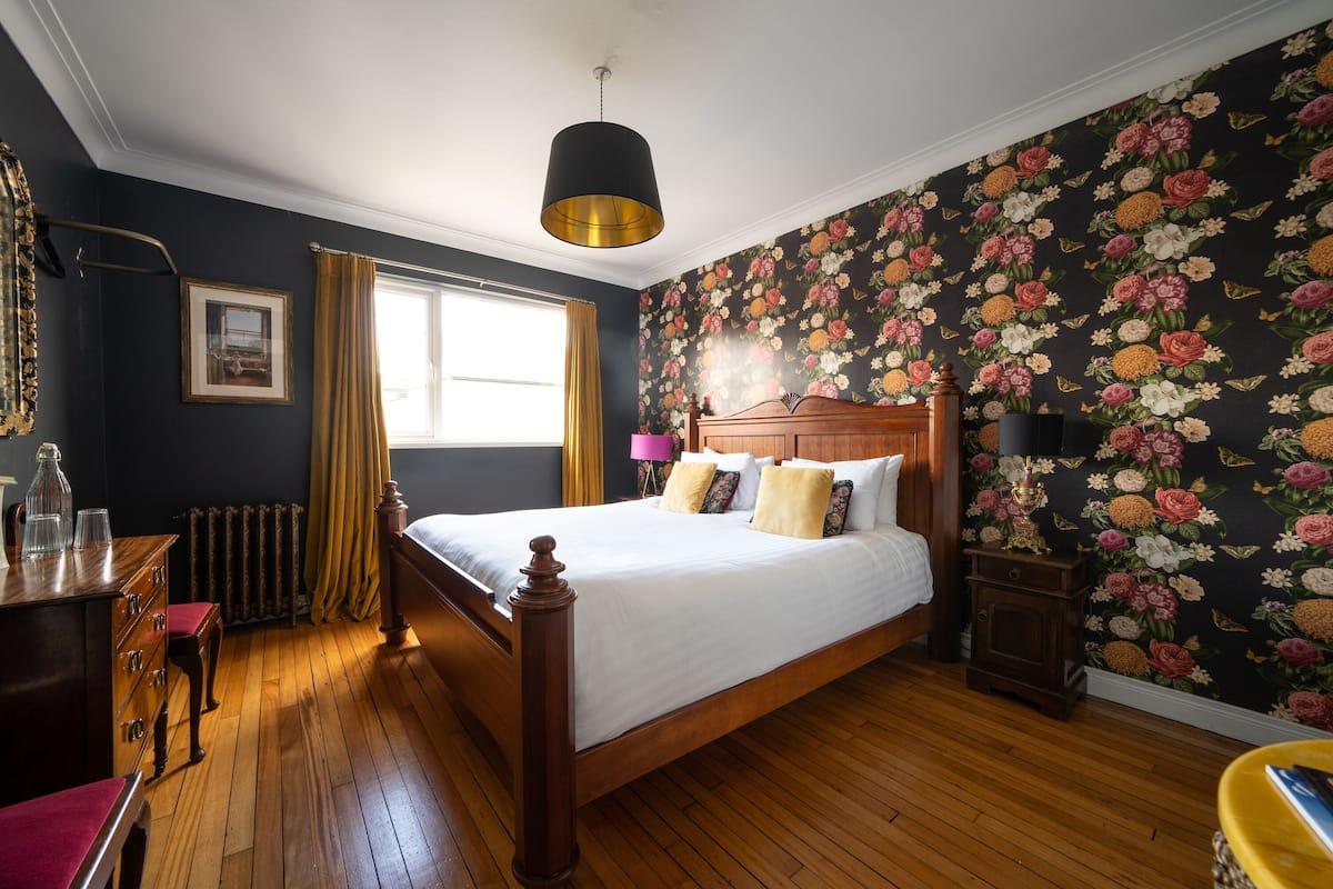 A bedroom with a wooden bed, a dresser, a nightstand, a lamp, and a window with curtains.
