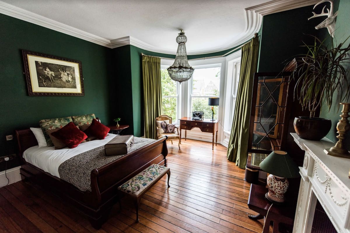 A bedroom with a large bed, a desk, a chandelier, and a fireplace.
