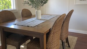 Une salle à manger avec une table en bois, des chaises en osier, un vase orné de verdure et des tableaux encadrés accrochés au mur.