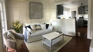 Un salon avec un canapé blanc, une table basse et un fauteuil. Un tapis recouvre le sol, et on peut voir une plante.