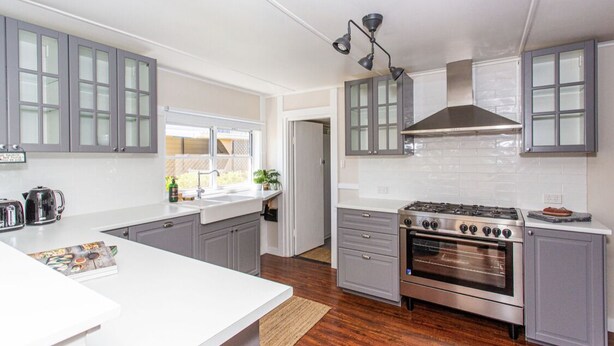 Une cuisine moderne avec des meubles gris, un plan de travail blanc, une cuisinière en acier inoxydable et une fenêtre.