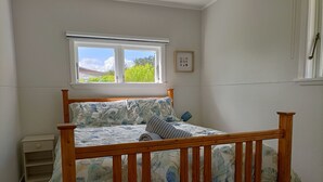 Een slaapkamer met een houten bed, een raam met uitzicht op groen en een klein nachtkastje.