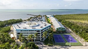 Um hotel com piscina no terraço, quadras de tênis e vista para o oceano.
