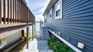 A narrow outdoor corridor with a wooden deck and steps leading to a house with a gray siding exterior. - Petit Retreat: The sweetest place on the Lake! (Seneca Falls)