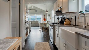 A modern kitchen with white cabinets, a dining area with a view, and a cozy seating area. - Petit Retreat: The sweetest place on the Lake! (Seneca Falls)
