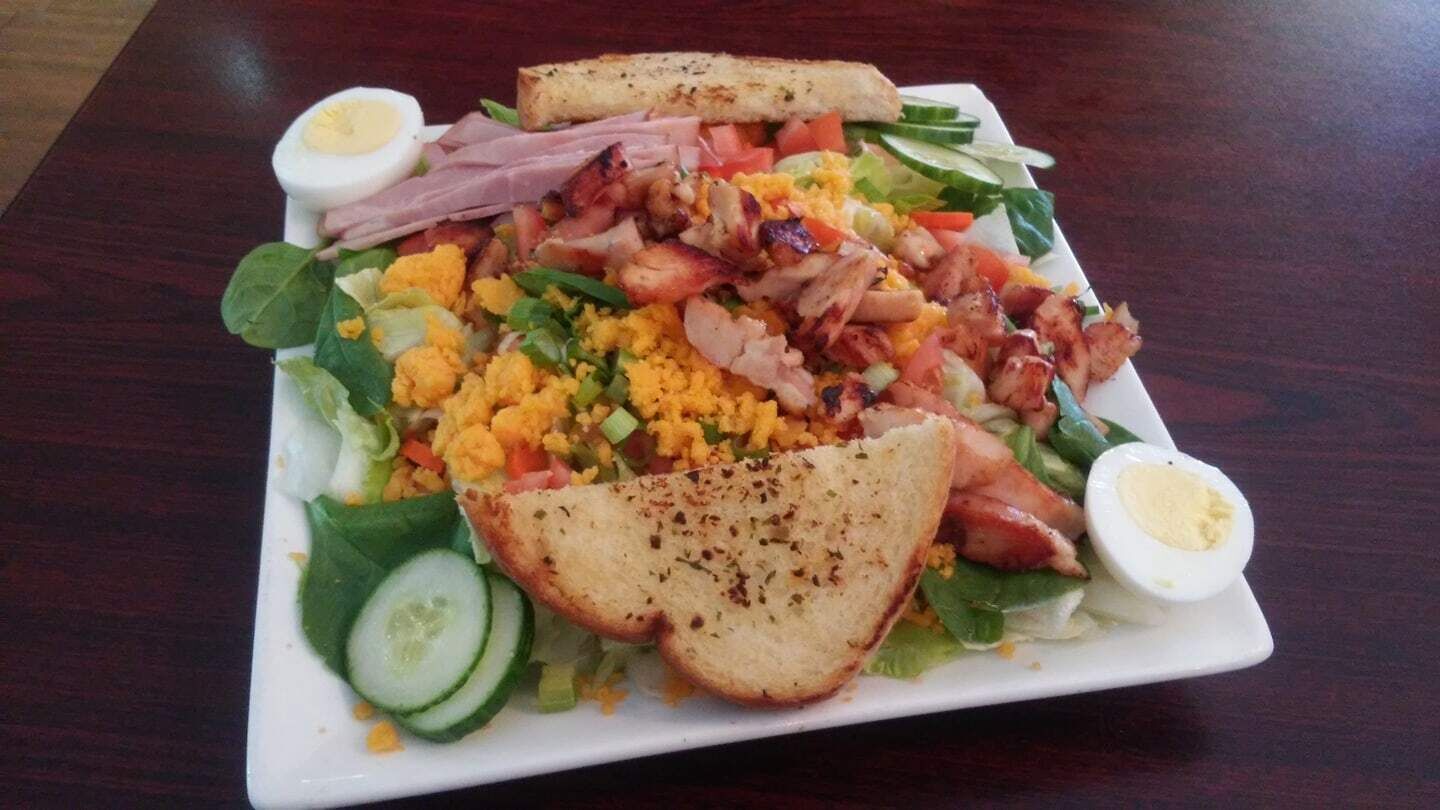 En hvid, firkantet tallerken med salat, røræg, bacon og to halve kogte æg på et træbord.