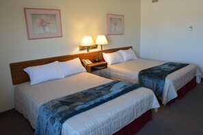 A hotel room with two single beds, each with a bedside table, a lamp, and a phone. There are framed floral pictures on the wall.