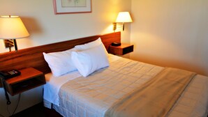 A hotel room with a bed, two bedside tables, a nightstand, a lamp, and a telephone. - Whitewood Inn (Whitewood)