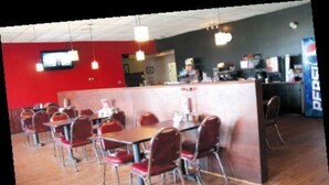 A restaurant with multiple tables and chairs, a counter, and a Pepsi vending machine. - Whitewood Inn (Whitewood)