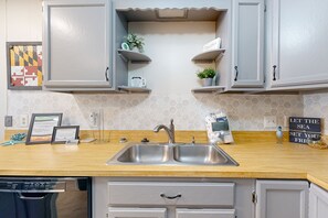 Experience a clean and inviting kitchen with a stainless steel sink, light grey cabinetry, and a wooden countertop.