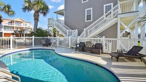 Piscina com um deck branco, espreguiçadeiras e uma escadaria que leva a uma varanda.