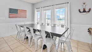 Uma sala de jantar com uma mesa grande e cadeiras brancas, uma bandeira na parede e uma decoração de âncora.