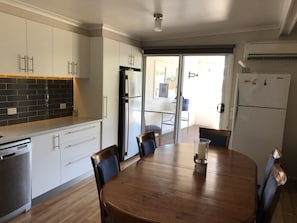 Une cuisine moderne avec des meubles blancs, un pare-feu noir en carreaux, des appareils en acier inoxydable et une table à manger en bois avec des chaises.
