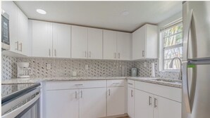 Uma cozinha moderna com armários brancos, uma geladeira de aço inoxidável e um painel de fundo padronizado.