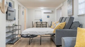 Quarto compacto com uma cama, um sofá cinza e uma mesinha.