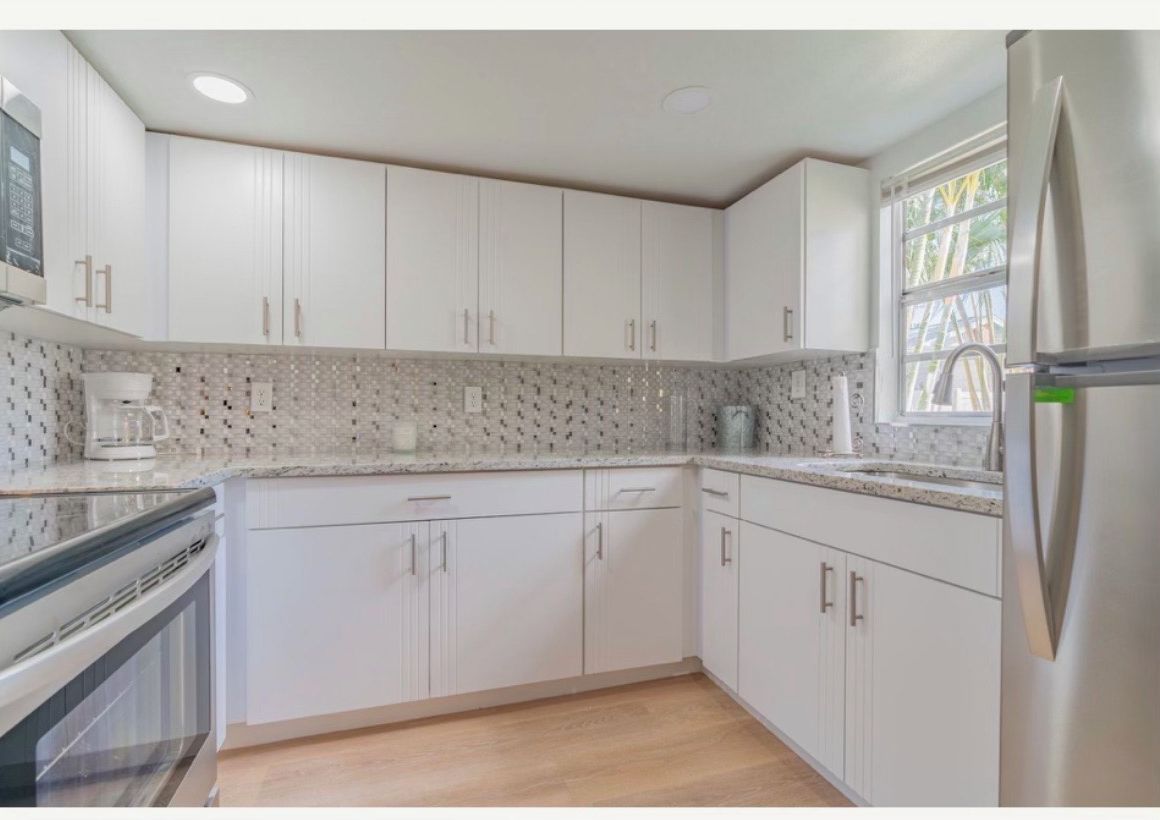 Una cucina moderna con mobili bianchi, un frigorifero in acciaio inossidabile e una parete di fondo decorata.