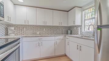 Una cucina moderna con mobili bianchi, un frigorifero in acciaio inossidabile e una parete di fondo decorata.