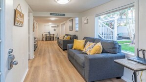 Uma sala de estar moderna com um sofá cinza e almofadas amarelas, piso de madeira e vista para uma escadaria branca que dá para o exterior.