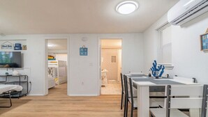 Quarto moderno e bem iluminado com área de refeições, televisão e uma cama beliche ao fundo.