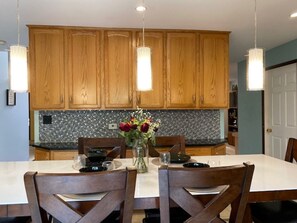A dining area with wooden cabinets, a tiled backsplash, and pendant lights.
