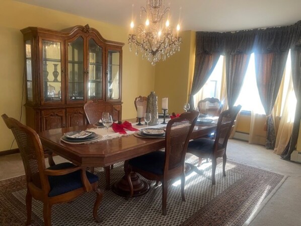 A dining room with a wooden table set for four, surrounded by chairs. A large wooden cabinet with glass doors is to the left.