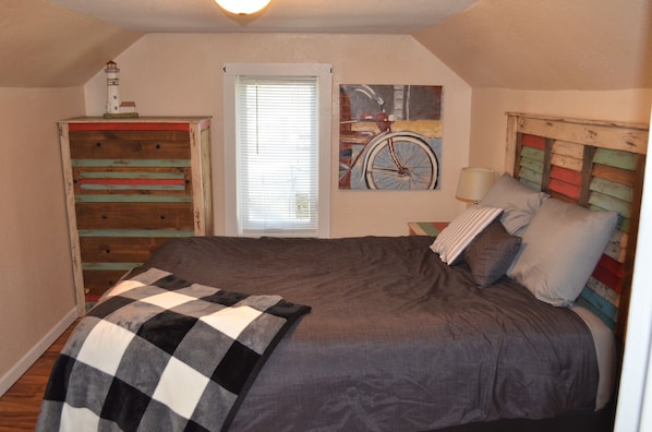 A bedroom with a large bed, a dresser, a window with blinds, and a bicycle painting on the wall.