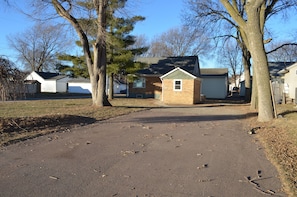 A residential driveway leading to a house with a garage, surrounded by trees and a clear sky.