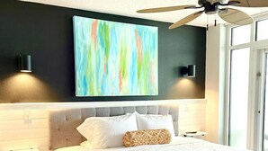 Een moderne slaapkamer met een groot bed, een plafondventilator en een kleurrijk abstract schilderij aan de muur.