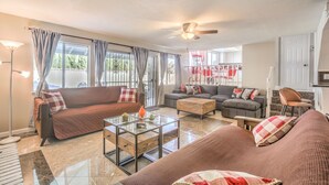 A spacious living room with a brown sofa, a grey sofa, and a glass coffee table. There is a ceiling fan and a large window with curtains. - The  Oasis (Las Vegas)