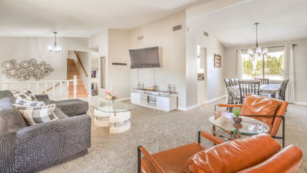 A spacious living room with a gray sofa, a glass coffee table, and a leather armchair. A flat-screen TV is mounted on the wall, and a dining area with a table and chairs is visible in the background. - The  Oasis (Las Vegas)