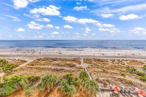 Ein Strand mit einer Holzpromenade, die zu Liegestühlen und Sonnenschirmen führt.