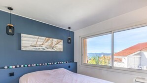 A bedroom with a bed, a large window, a wall-mounted artwork, and a string of decorative balls. - La Corniche by Interhome (Saint Cyr sur Mer La Madrague)
