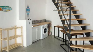 A modern kitchen with a built-in washing machine, a wooden staircase, and a small wooden shelf unit. - La Corniche by Interhome (Saint Cyr sur Mer La Madrague)