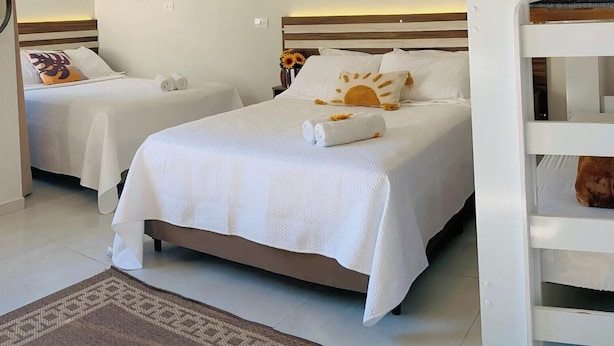 A hotel room with two single beds, a large bed, and a small table with towels. - Pousada Villa Vantino (Penha)