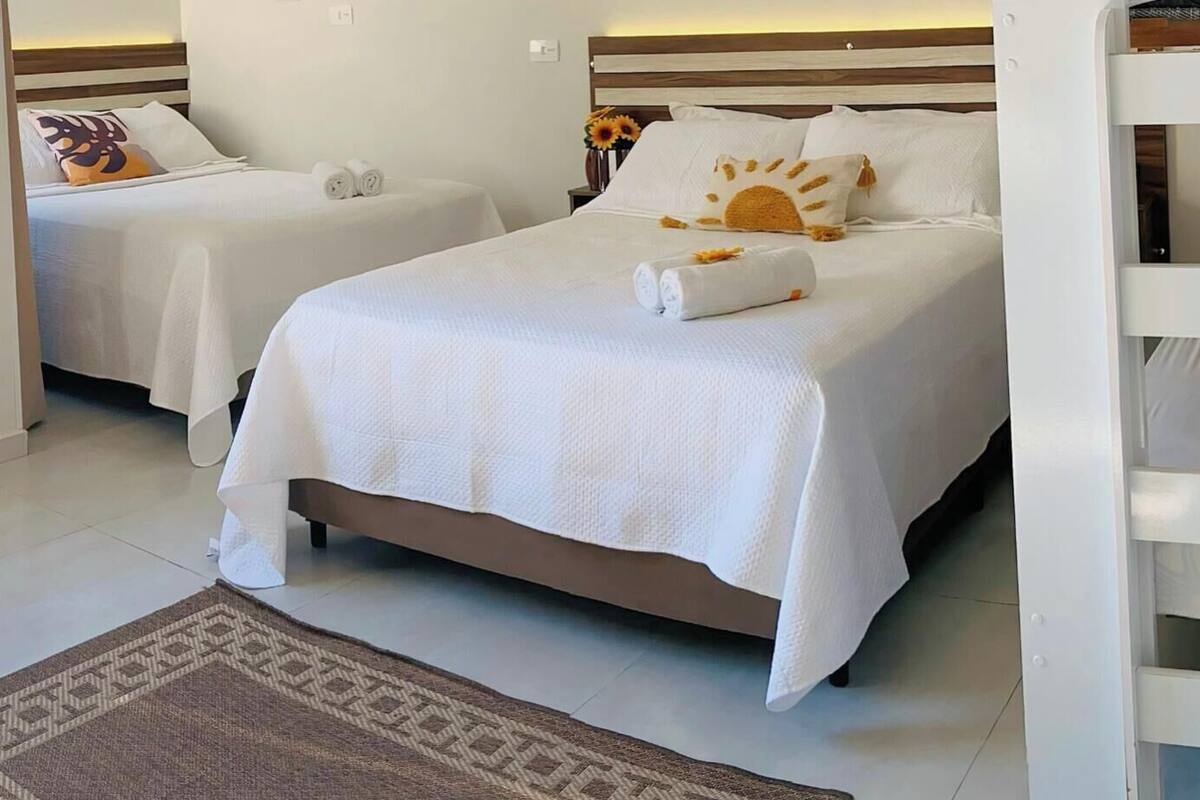 A hotel room with two single beds, a large bed, and a small table with towels.