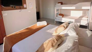 Habitación de hotel con una cama individual, un televisor montado en un panel de madera, una cama litera al fondo y un equipo de aire acondicionado en la pared.
