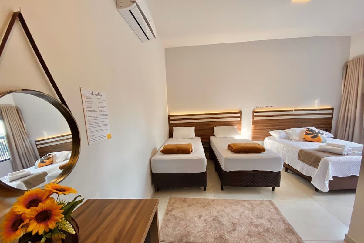 A hotel room with two single beds, a wooden desk, a mirror, a wall-mounted air conditioner, and a bulletin board.