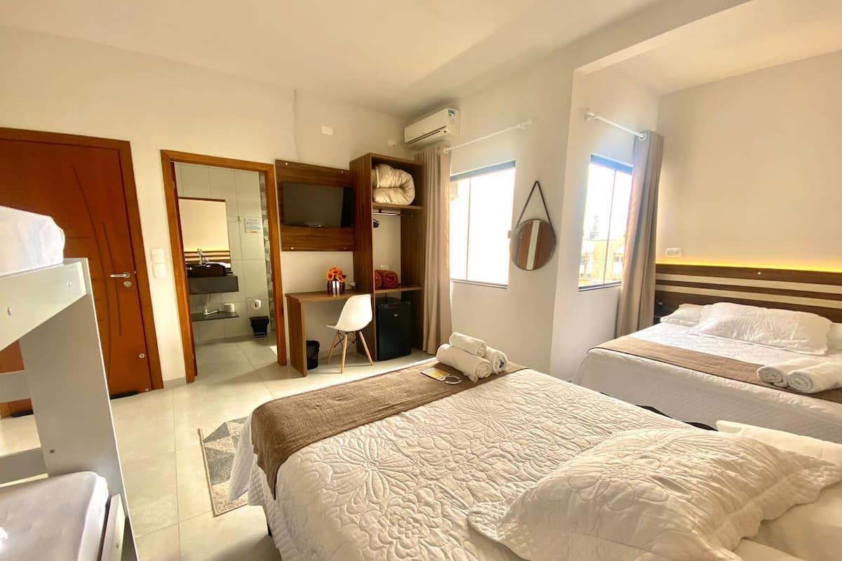 A hotel room with two beds, a kitchenette, a mirror, and a TV.