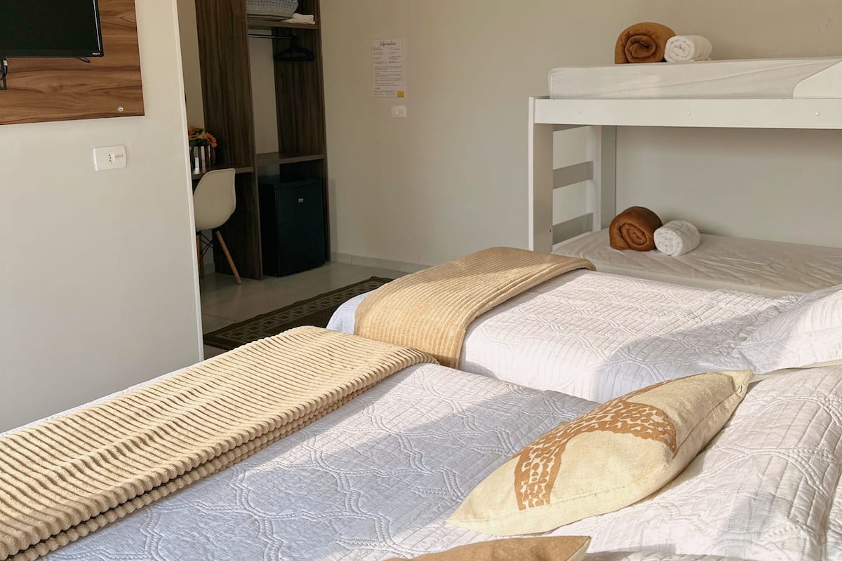 A hotel room with two beds, a wardrobe, a desk, and an air conditioning unit.