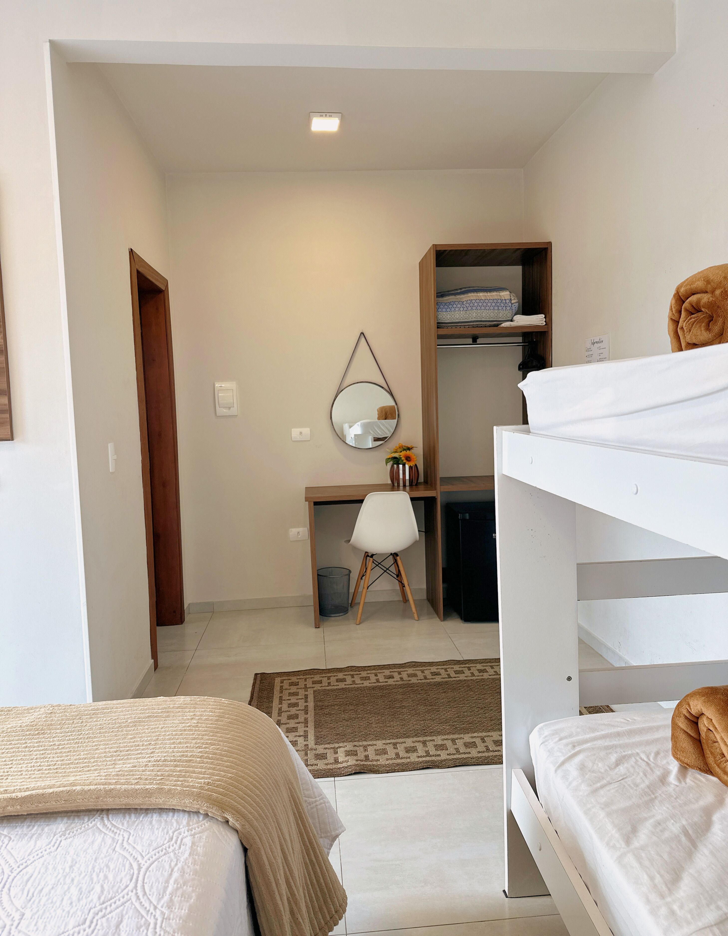 Une chambre à coucher de taille réduite, comprenant un lit superposé, un bureau avec une chaise, un miroir et une armoire.