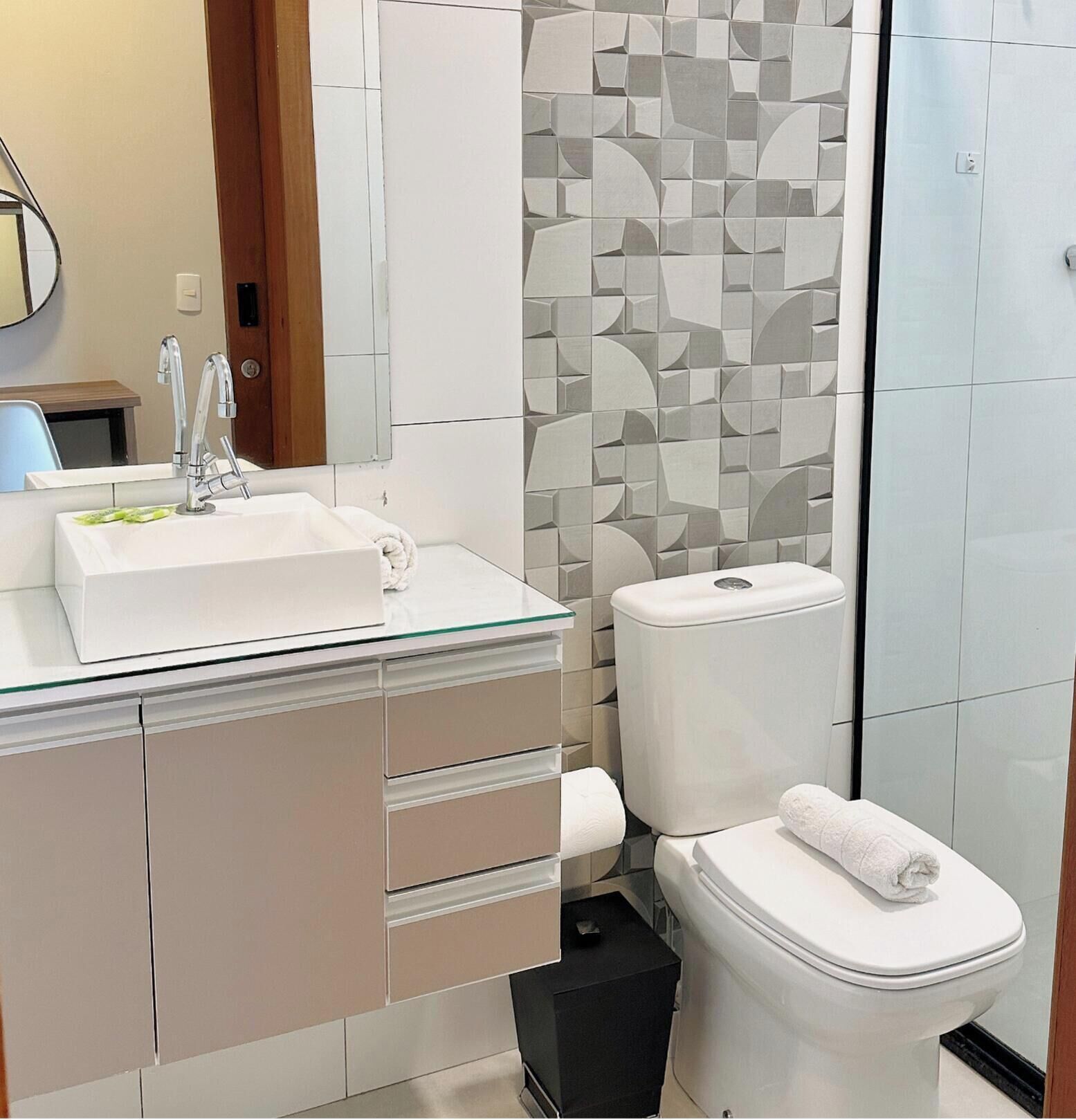 Uma casa de banho moderna com lavatório de vidro, armários bege, sanita e área de duche.