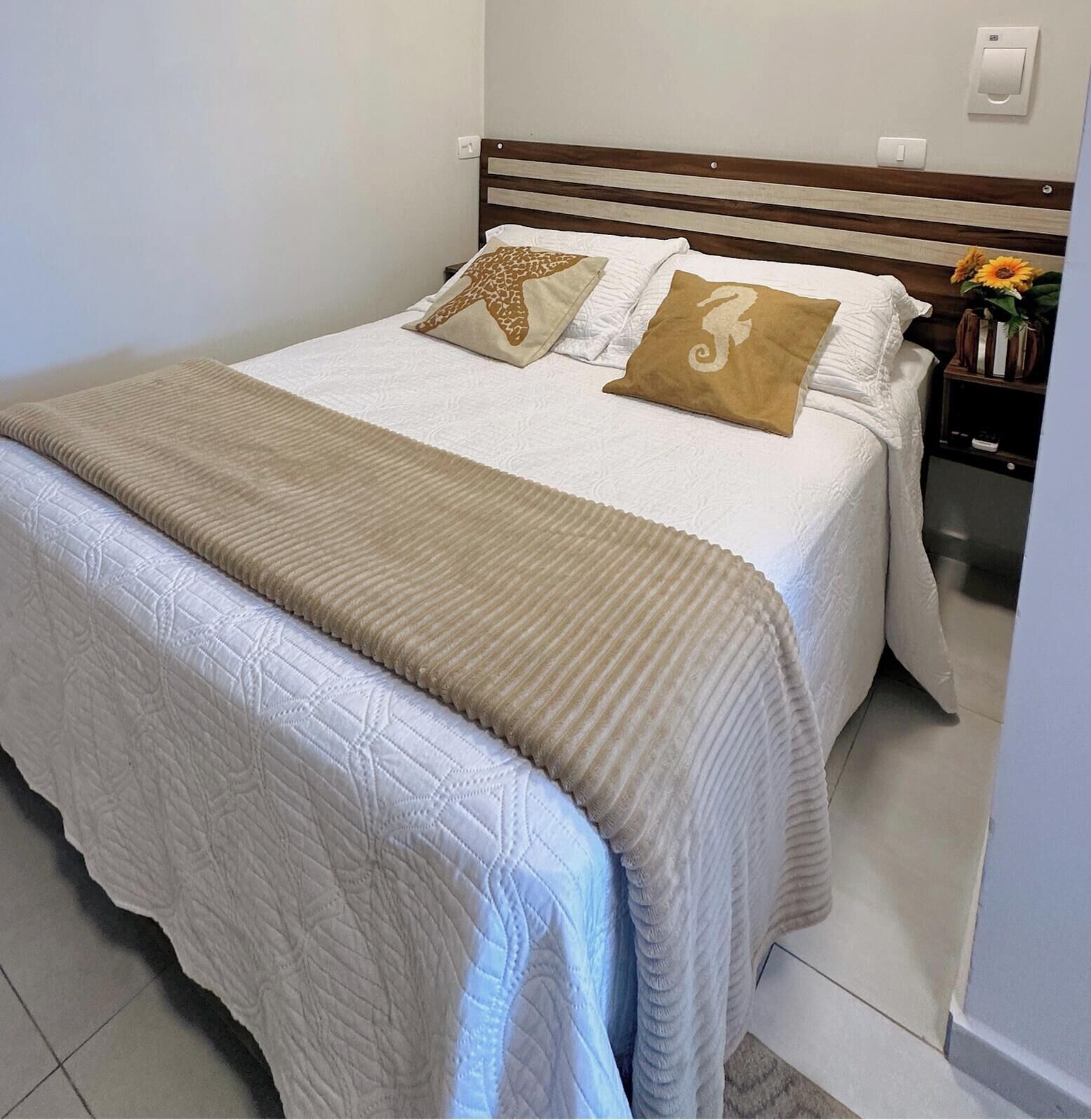 A neatly made bed with a white quilt, two decorative pillows, and a beige throw blanket.