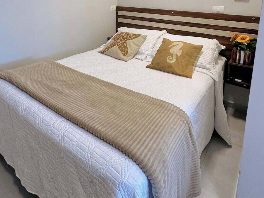A neatly made bed with a white quilt, two decorative pillows, and a beige throw blanket.